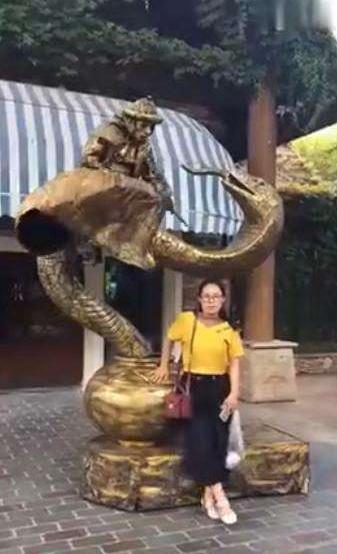 美女跟铜像合影，铜像却突然流出了水，美女转头一看被吓了一跳